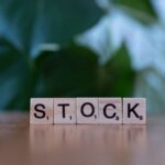 Close-up of wooden letter blocks spelling 'STOCK' on a table against a blurred green background.