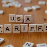 Wooden tiles spelling 'USA' and 'TARIFFS' on a wooden surface symbolizing trade issues.
