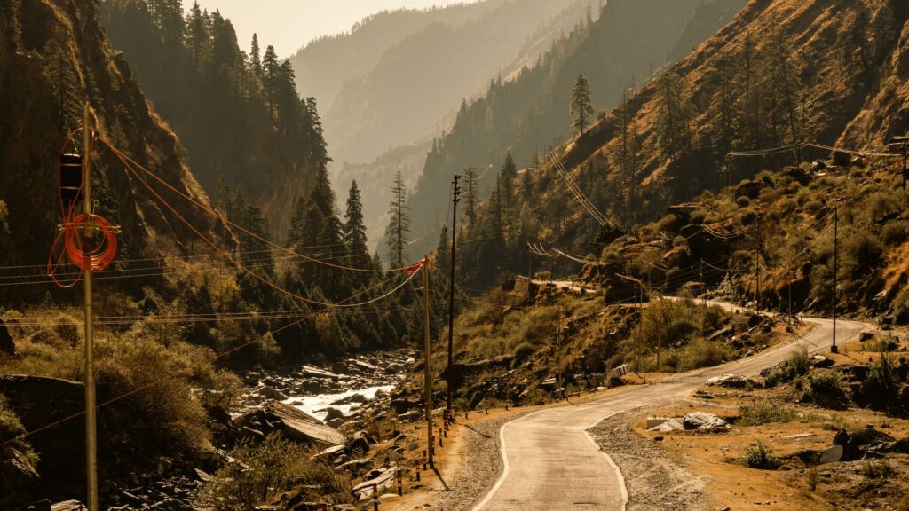 Breathtaking view of mountain road in Harsil, Uttarakhand, with lush forests and power lines.