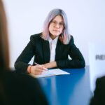 A young woman with dyed hair takes notes during a job interview.