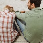 A couple sitting on the street, engaged in a distressed conversation, capturing a moment of emotional tension.
