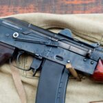 A detailed view of a military rifle with ammunition on a canvas backdrop.