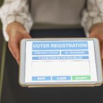 Close-up of hands holding a tablet displaying digital voter registration form.