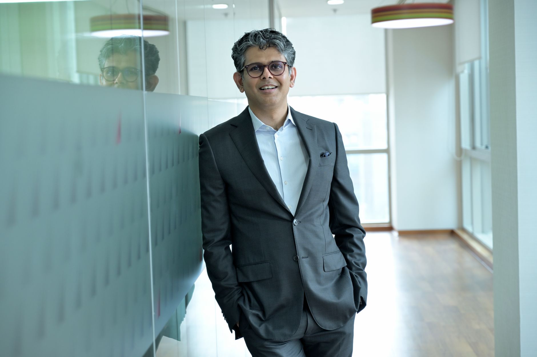 Smiling businessman standing confidently in a modern office hallway, wearing a suit.