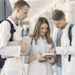 Three medical students in a hallway discussing notes, fostering teamwork and learning.