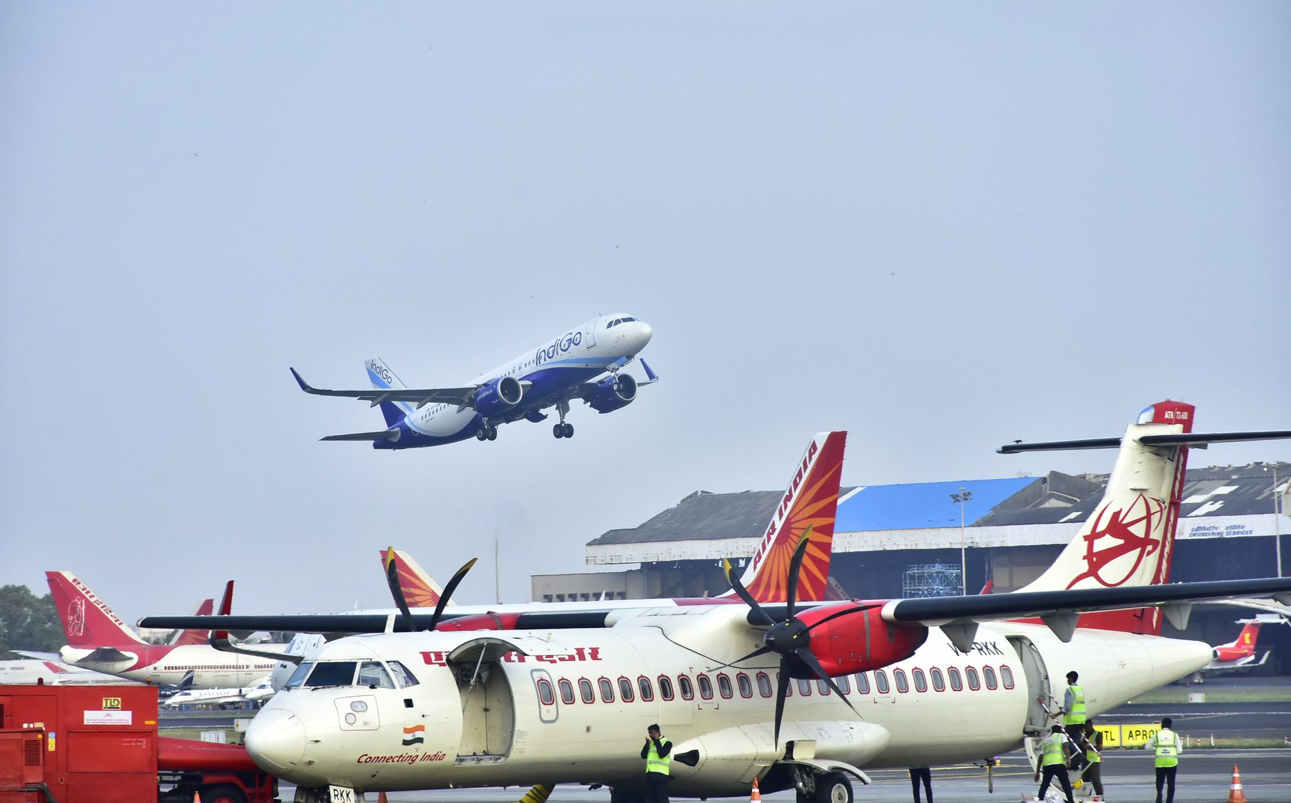 Airplanes on tarmac with one taking off at a busy airport on a clear day.