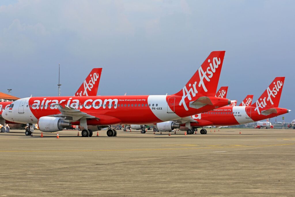 Multiple AirAsia planes stationed at an airport with clear skies in the background.