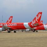 Multiple AirAsia planes stationed at an airport with clear skies in the background.