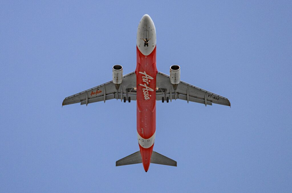 Low-angle shot of an AirAsia airplane flying against a bright blue sky.