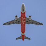 Low-angle shot of an AirAsia airplane flying against a bright blue sky.