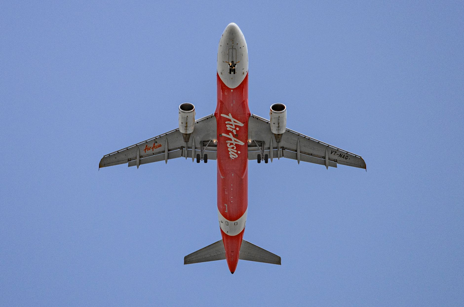Low-angle shot of an AirAsia airplane flying against a bright blue sky.
