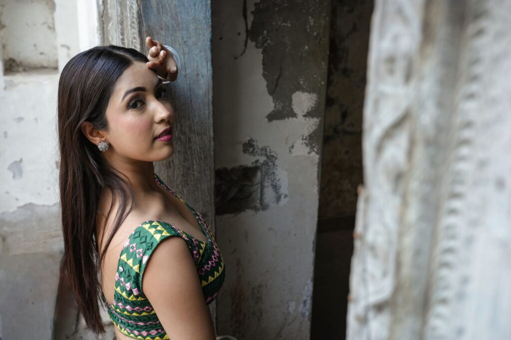 Portrait of a woman in a colorful traditional outfit posing in an aged, rustic interior.