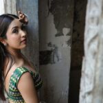 Portrait of a woman in a colorful traditional outfit posing in an aged, rustic interior.