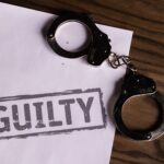 Top view of handcuffs on paper with 'GUILTY' text, symbolizing a verdict or crime.