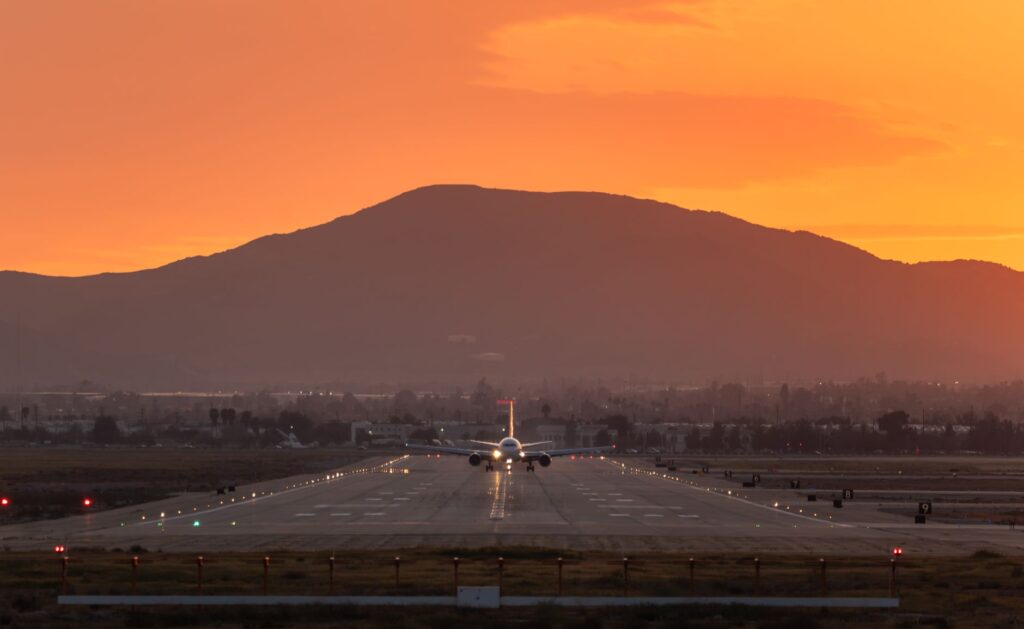 A cargo plane landing on a San Bernardino runway during sunset with mountains in the background.