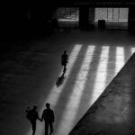 Silhouette of people walking under sunlight inside a large building.