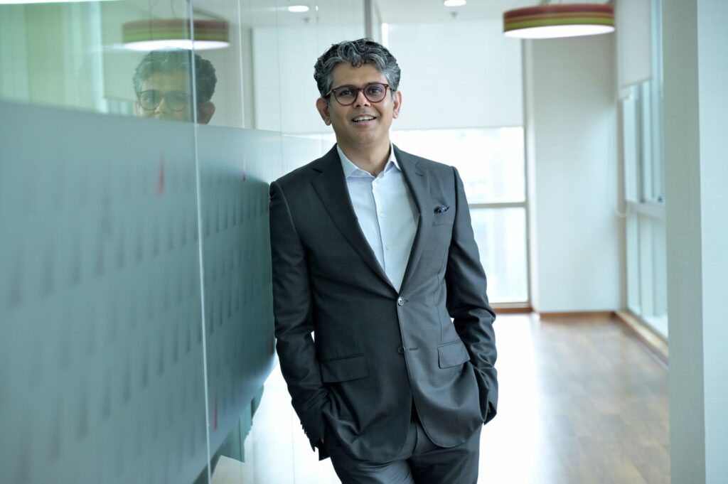 Smiling businessman standing confidently in a modern office hallway, wearing a suit.