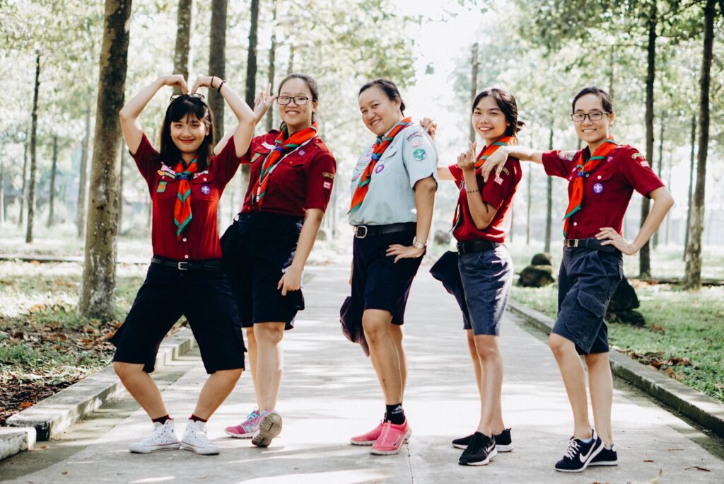 A cheerful group of scouts posing in a park with vibrant uniforms and energetic gestures.