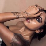 Close-up portrait of a tattooed woman with eye makeup and red lips posing in an editorial shoot.