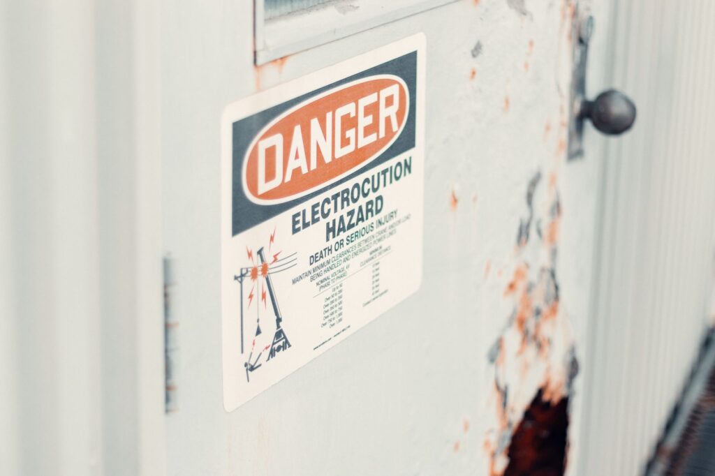 Close-up of a danger sign warning of electrocution hazard on a rusty utility door, indicating safety precautions.