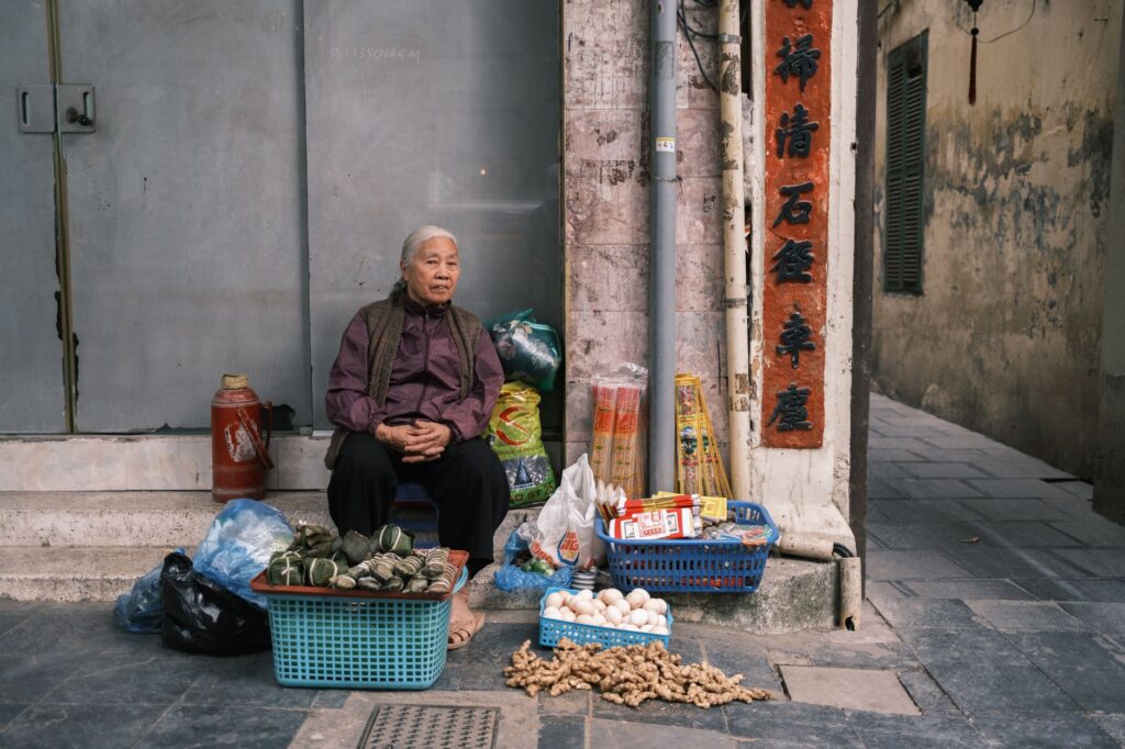 Elderly woman selling fresh produce on a city street, showcasing local culture.