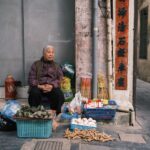 Elderly woman selling fresh produce on a city street, showcasing local culture.
