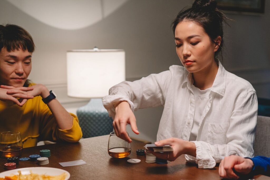 Two friends play poker with chips and whiskey on a wooden table.