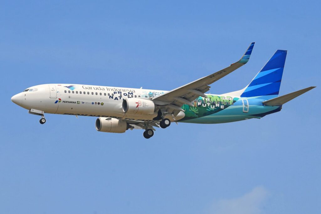 Garuda Indonesia Boeing 737 aircraft flying against a clear blue sky, showcasing vibrant livery.