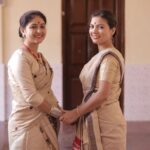 Two South Asian women in traditional sarees smiling indoors, reflecting Indian cultural attire.