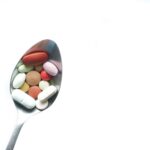 A variety of colorful pills and tablets resting on a spoon on a white background.