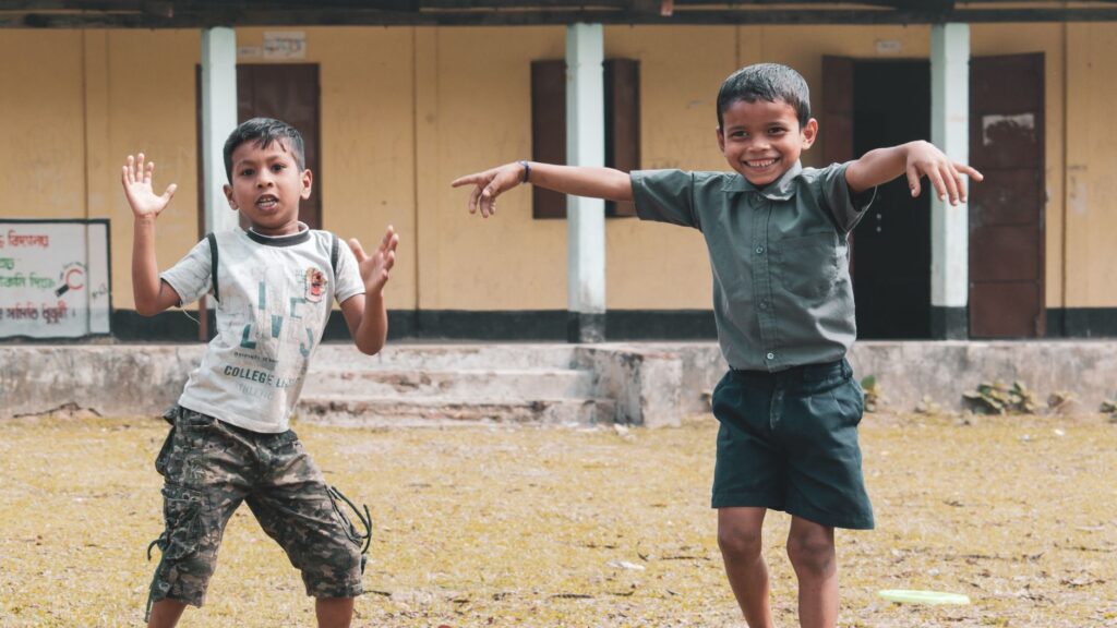 Two boys happily play outside a rural school in Assam, India, showcasing the joy of childhood and friendship.