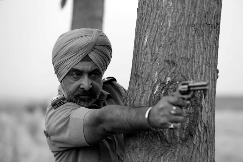Black and white image of a police officer in uniform aiming a revolver behind a tree.