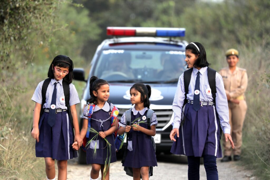 Schoolgirls in uniforms walk safely alongside a police escort on a rural road.