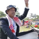 An Asian man giving a speech at an outdoor rally, gesturing with his hand.