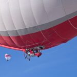 Colorful hot air balloon soaring in a clear blue sky during a vibrant festival in Château-d’Œx, Switzerland.