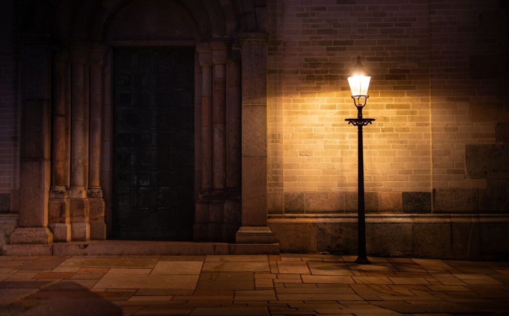 A dimly lit street lamp illuminates a medieval church entrance, creating an atmospheric night scene.