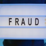 Close-up of hands holding a sign with 'fraud', illuminated in blue light.