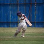 A young cricketer in action on a sunny day, playing on a grass field with a bat and wicket.