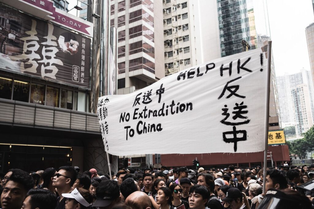 Protesters in Hong Kong holding banners against extradition to China, urban backdrop.