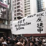 Protesters in Hong Kong holding banners against extradition to China, urban backdrop.