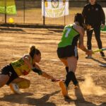 Action-packed field hockey match captured on a dusty outdoor field during the day.