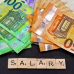 Euro banknotes alongside wooden Scrabble letters spelling 'salary' symbolize financial earnings and payroll.