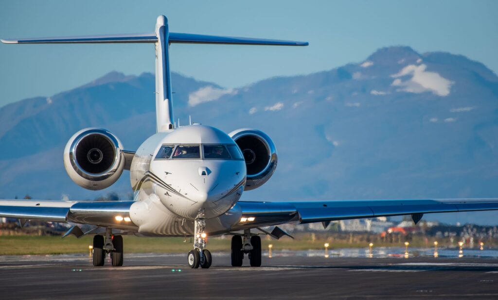 A sleek private jet on the runway with scenic mountains in the background under a clear blue sky.
