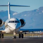 A sleek private jet on the runway with scenic mountains in the background under a clear blue sky.