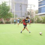 A young soccer player in action kicking the ball on an outdoor field surrounded by teammates.
