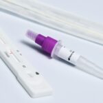 Close-up of a COVID-19 rapid antigen test kit featuring a swab, dropper, and test strip on a white surface.