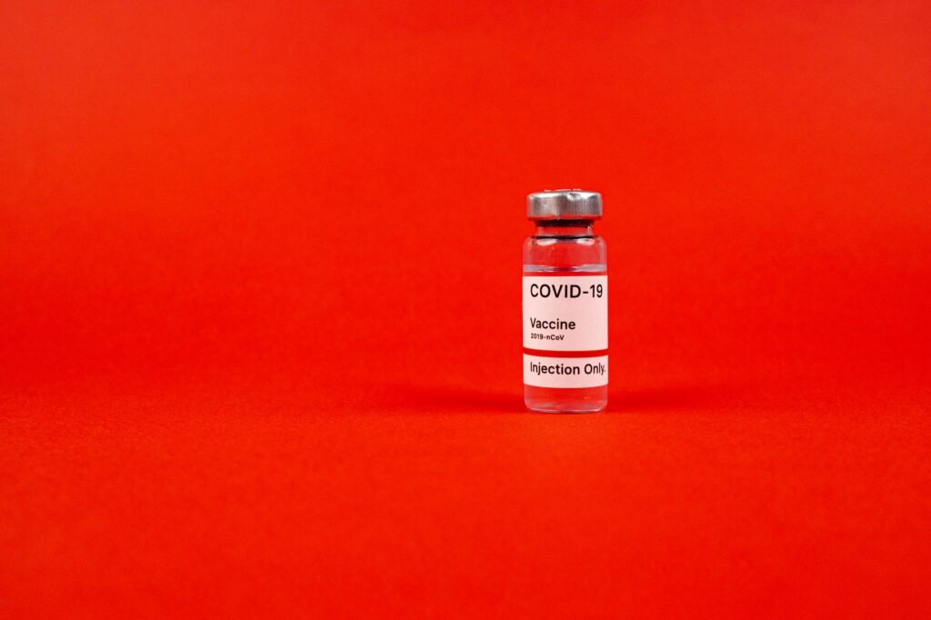 Glass vial of COVID-19 vaccine on a vibrant red backdrop, emphasizing protection.