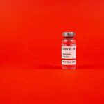 Glass vial of COVID-19 vaccine on a vibrant red backdrop, emphasizing protection.