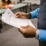 An instructor examining test papers in a classroom setting, focusing on education and evaluation.
