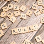 Wooden letter tiles arranged to spell 'Rules' on a textured wooden background.